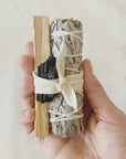 Ritual-Set Protection mit Palo Santo, weisser Salbei, Turmalin Edelstein mit Baumwollband in der Hand liegend